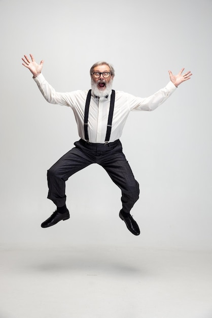 Portrait of funny joyful senior man professor teacher jumping isolated over gray background