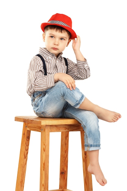 Photo portrait of a funny little boy sitting on a high stool in a red hat isolated