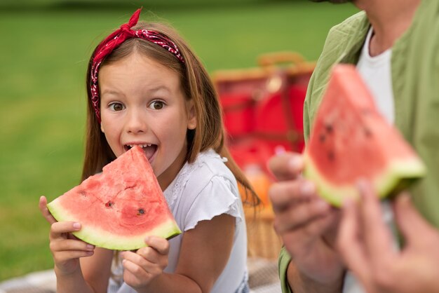 Ritratto di una bambina divertente che guarda la telecamera mentre mangia anguria con la famiglia del padre