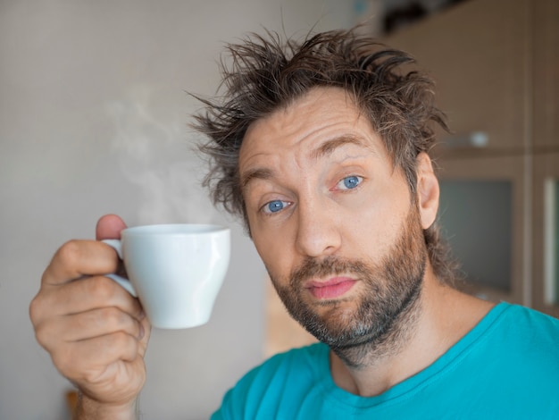 Portrait of a funny man after awakening with a cup of hot coffee or tea