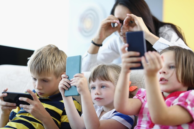 Portrait of funny mother watching over kids concentrated children holding smartphones and