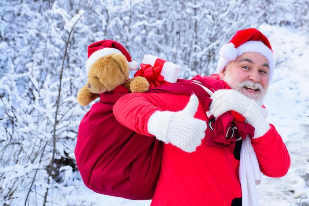 Portrait of funny santa with gift on christmas eve outside  thumbs up sign