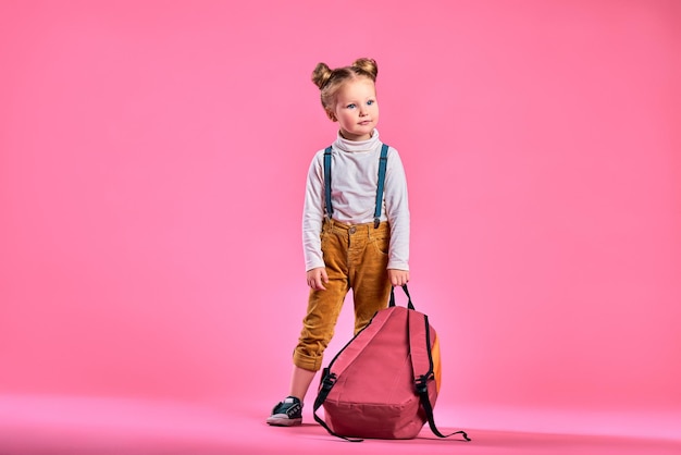 Portrait of a funny schoolgirl with pink backpack over pink background Copy space