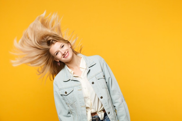 Photo portrait of funny smiling young woman in denim casual clothes with fluttering hair looking camera isolated on yellow orange wall background in studio. people lifestyle concept. mock up copy space.