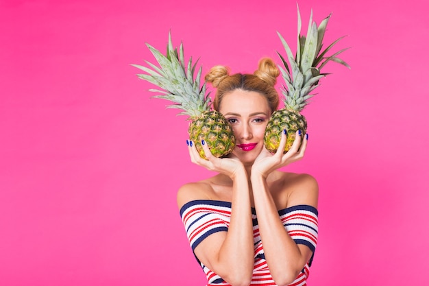 Portrait of funny woman and pineapple over pink background with copyspace.