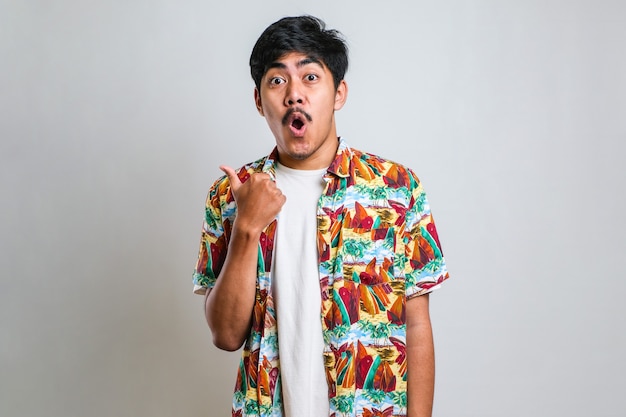 Портрет забавного молодого азиатского человека в белой футболке, улыбающегося и указывающего на то, чтобы представить что-то на его стороне, на красном фоне с копией пространства