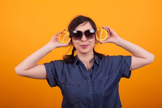 Portrait of funny young woman holding juicy oranges in studio over yellow background. Portrait of pretty cheerful girl holding tasty oranges.