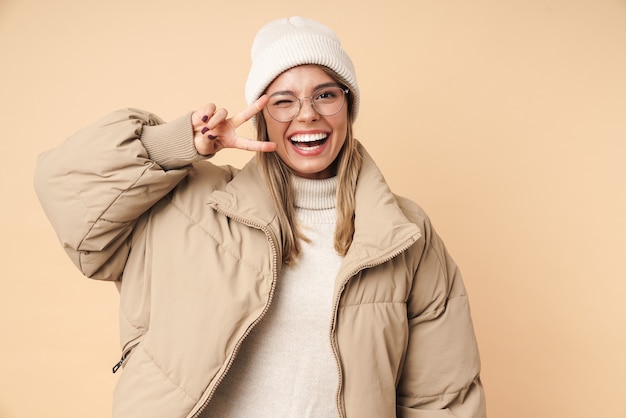 Portrait of funny young woman in winter coat winking and gesturing peace sign 