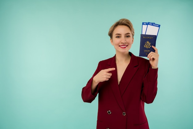 Портрет смешной молодой женщины с паспортом и посадочным талоном на синем фоне. Открытие границ. Начало авиаперелетов после пандемии.