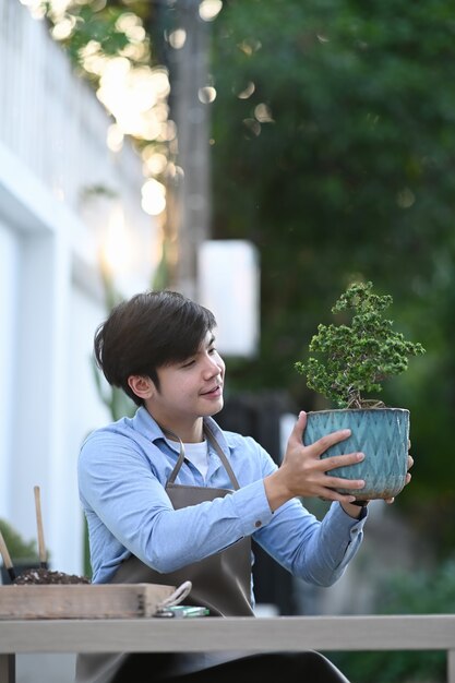 웃 고 그의 집 정원에 앉아있는 동안 분재 나무 냄비를 들고 정원사 남자의 초상화.