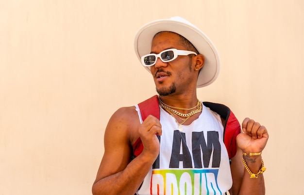 Portrait of a gay black ethnic man at the pride party on a cream wall LGBT flag