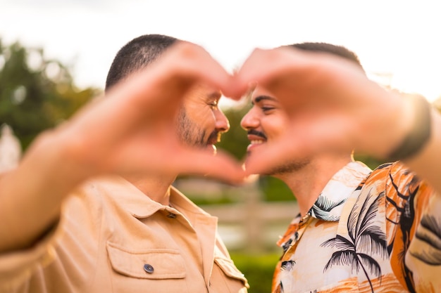 Foto ritratto di ragazzo e ragazza gay che fanno il gesto del cuore o dell'amore al tramonto in un parco della città concetto di diversità e lgbt