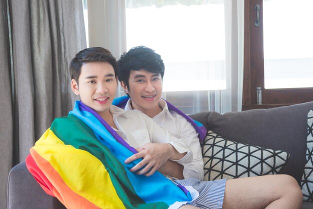 Photo portrait of gay couple holding rainbow flag while relaxing on sofa at home