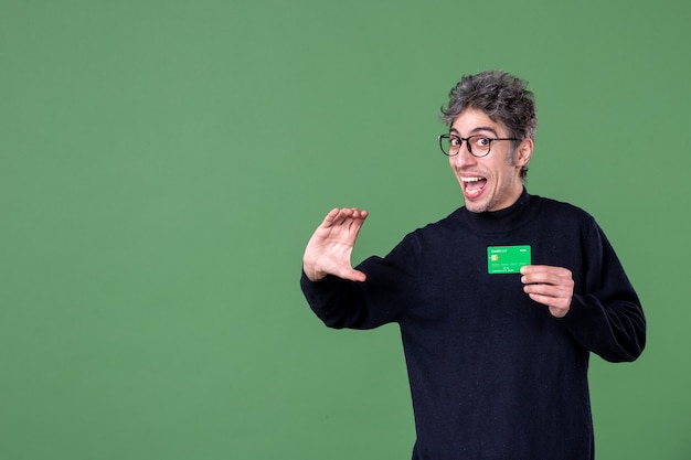 スタジオショットの緑の壁でクレジットカードを保持している天才男の肖像画
