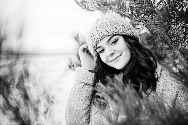 Portrait of gentle girl in gray coat and hat against new year tree outdoor.