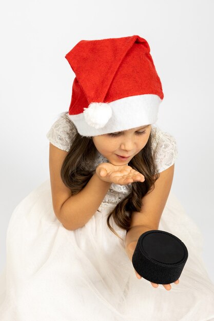 Foto ritratto di una ragazza gentile e gioiosa con un cappello di babbo natale che manda un bacio a un altoparlante musicale intelligente isolato su...