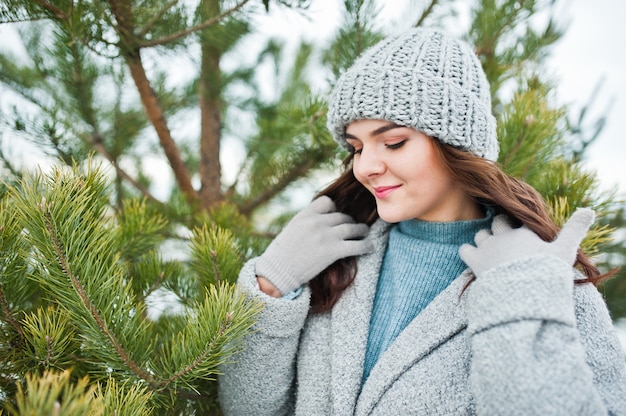 Portrait of gentle woman in gray coat and hat against christmas tree outdoor.