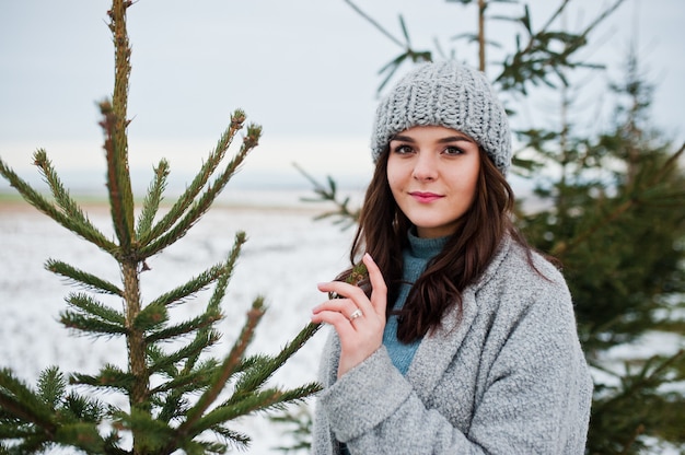 Ritratto della donna delicata in cappotto e cappello grigi contro l'albero di natale all'aperto.