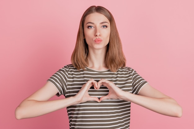 Photo portrait of gilrish dreamy lady fingers show heart gesture send blow air kiss on pink background