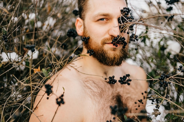 Portrait of ginger brutal naked man with beard posing among bushes