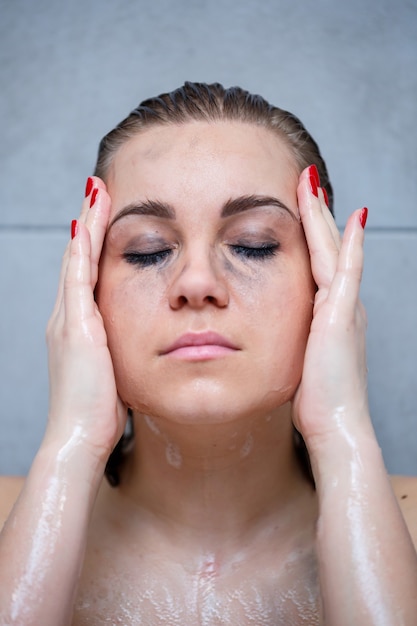 Portrait of a girl in a bath sitting and washing her face from makeup. Around the eyes are black spots from mascara. Close-up of a young woman erasing spots on her eyes