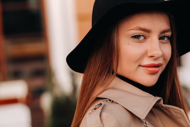 Portrait of a girl in a beige coat and black hat on a city street. Women's street fashion. Autumn clothing.Urban style.