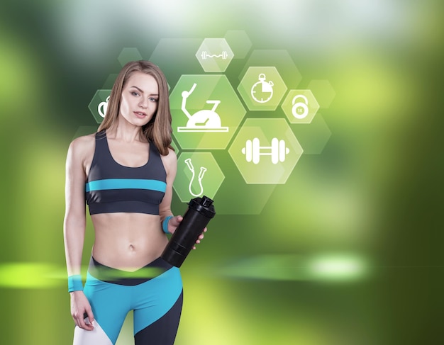 Portrait of a girl in black and blue sportswear holding her yoga mat and standing against a green background with sport icons. Mock up.