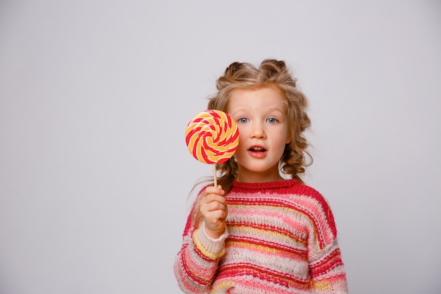 Portrait of a girl a blonde child with a Lollipop on a stick smiling in colored clothes