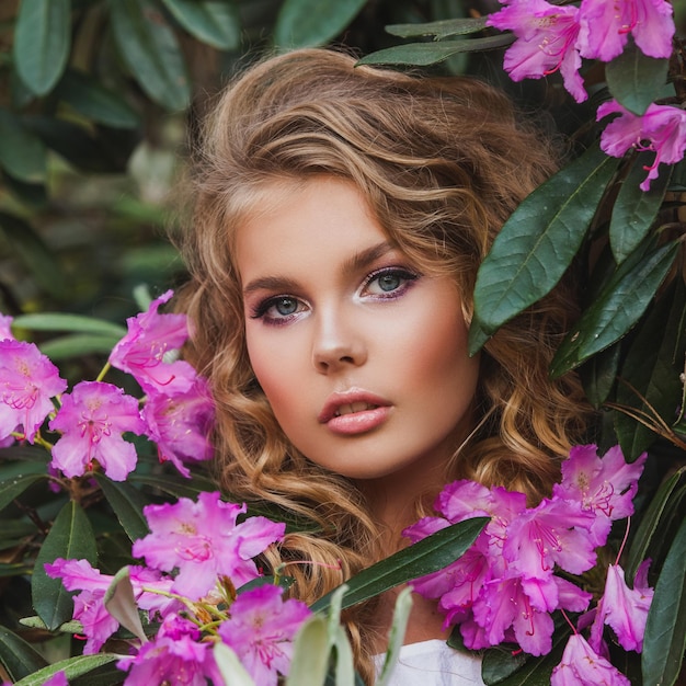 Portrait of a girl in a blooming garden A bush of flowers is rhododendron pink Beautiful hair and makeup