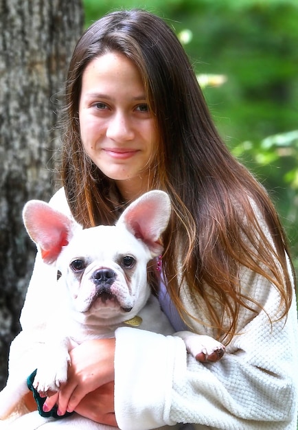 Photo portrait of girl carrying dog against plants