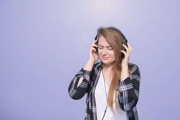 Portrait girl in casual clothing that is happy to listen to music in headphones on a purple background.Student girl listens to music in her headphones with closed eyes isolated on a purple background