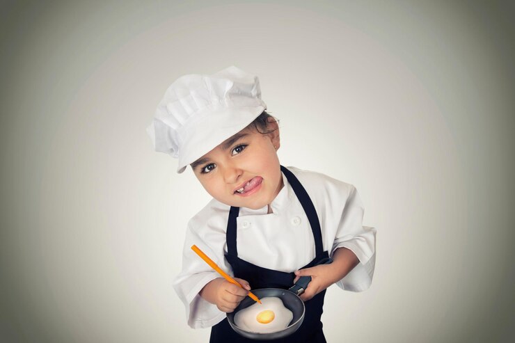 Photo portrait of girl in chef uniform preparing fried egg against white background
