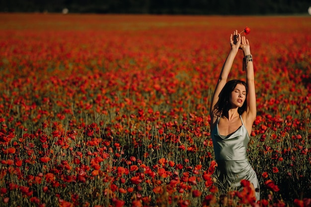 Portrait of a girl in a dress on a poppy field at sunset