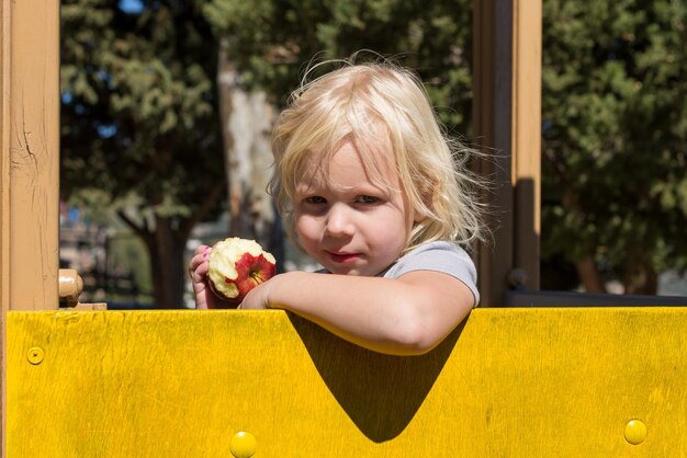 Portrait of girl eating apple while standing by wood