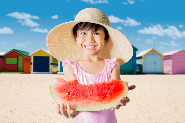 Portrait of girl eating watermelon while standing at beach against sky