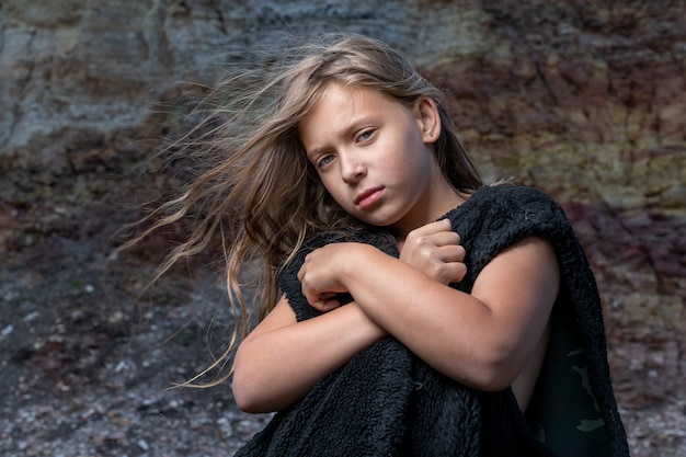Photo portrait of a girl in a fur sleeveless jacket at the foot of the cliff