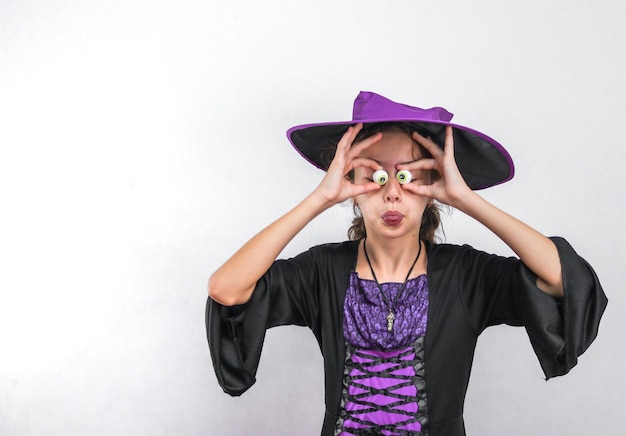 Portrait of a girl in a Halloween costume a hat holding candy over her eyes