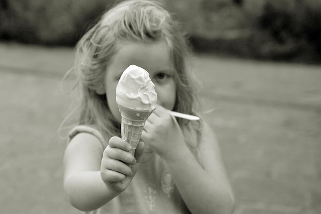 Foto ritratto di una ragazza che mangia un cono di gelato mentre è in piedi sul campo