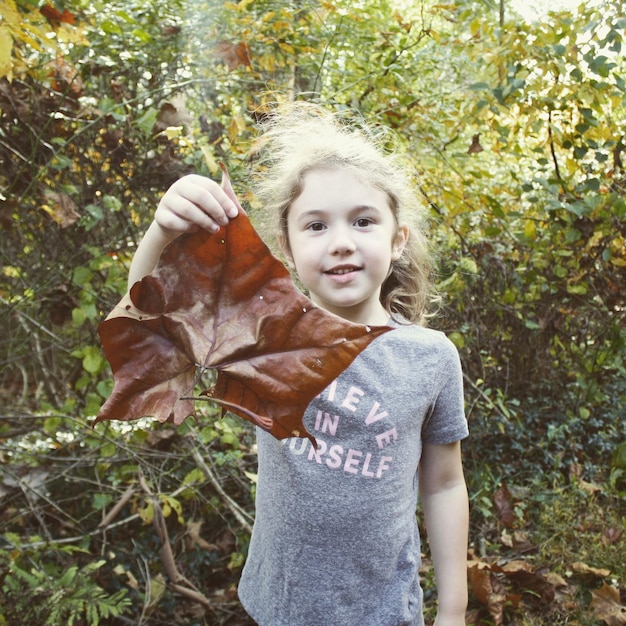 Photo portrait of girl holding leaf against trees