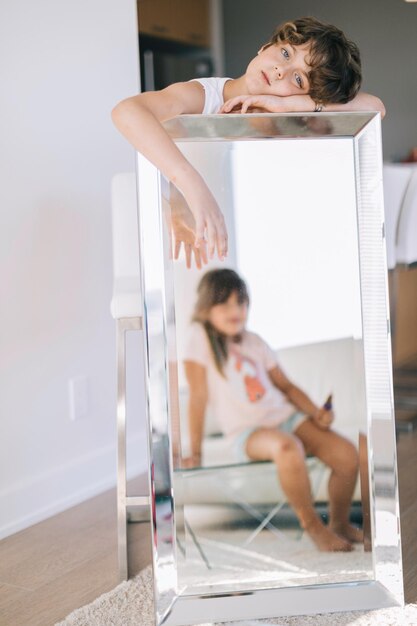 Portrait of girl holding mirror with reflection of sister at home