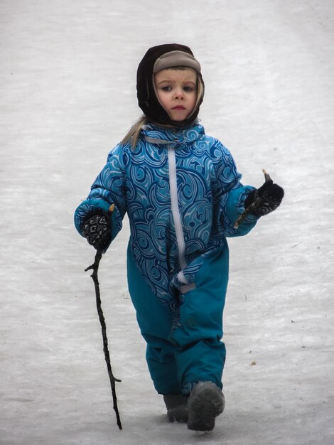 Portrait of girl holding stick walking on snow covered field