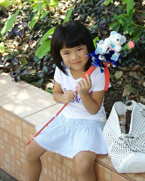 Portrait of girl holding toy on retaining wall