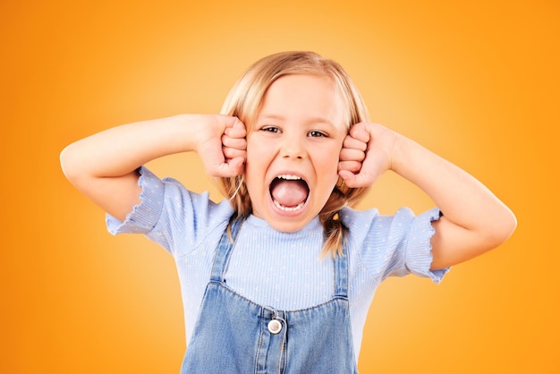 Portrait girl and kid with anger screaming or emoji with emotion on a yellow studio background Face person or model with stress frustrated or shouting with a child facial expression or attitude