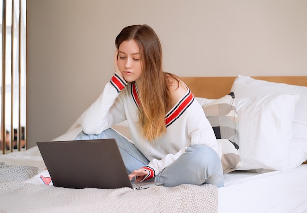 Portrait of a girl lying on the bed with a laptop