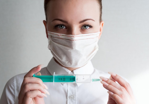 Portrait of a girl in a medical mask Holding a syringe in her hand Close upxA