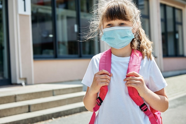 Foto ritratto di una ragazza con una maschera medica nel cortile della scuola per la protezione dei bambini e degli scolari