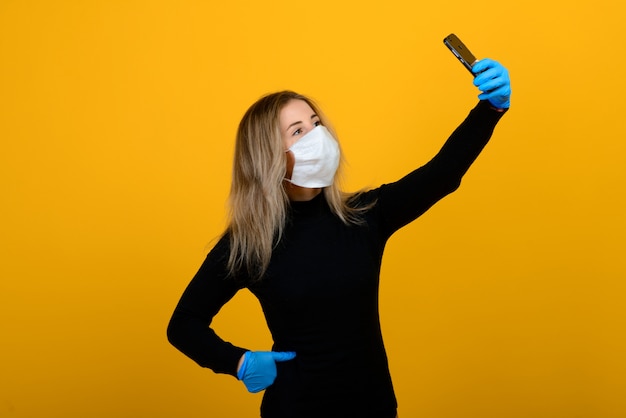 Portrait of a girl in a medical mask, which puts on a rubber glove. Yellow and grey background. Copy space.