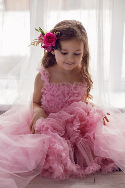 ピンクのドレスを着た女の子のポートレートと彼女の頭にバラとネットを持つ花がスタジオで撮影されています