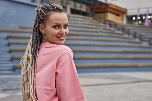 Photo portrait of a girl in a pink tshirt and with dreadlocks who looks directly into the camera against t...