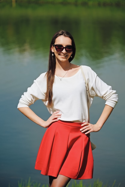 Portrait of a girl in red skirt and white blouse standing on river bank